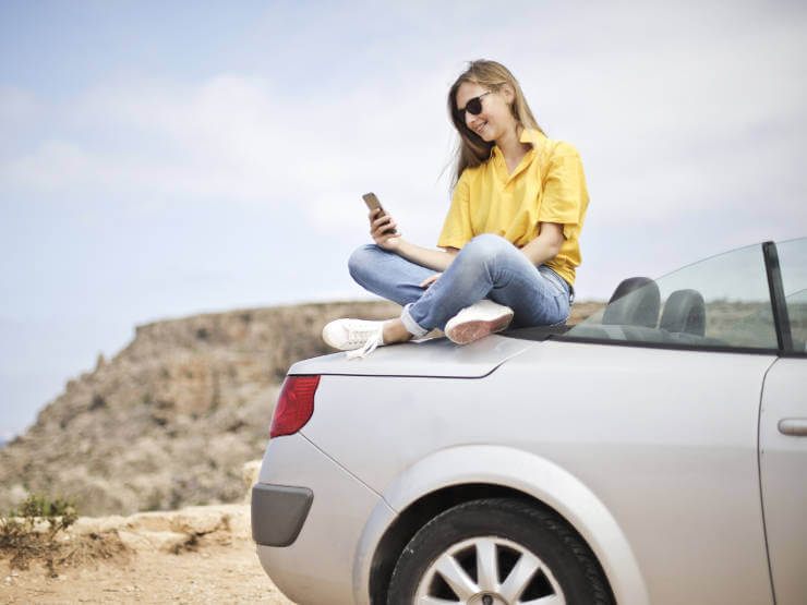 girl-sitting-on-car-using-mobile-phone-app